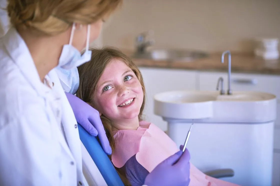 A young girl in an exam chair smiling beside a female dentist.