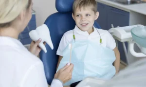 A young girl in an exam chair looking at her smile in a mirror next to a male dentist.