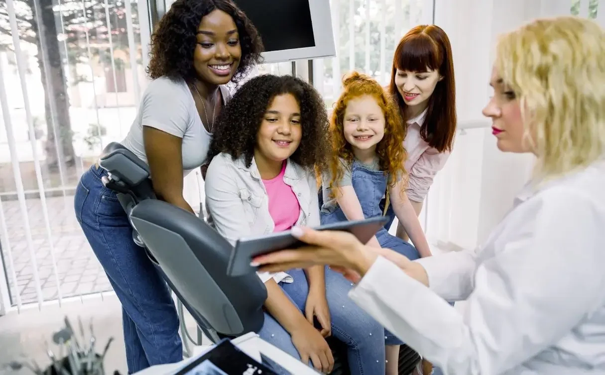 In a bright, family-friendly clinic, a dentist uses a tablet to explain dental care to children and their guardians.