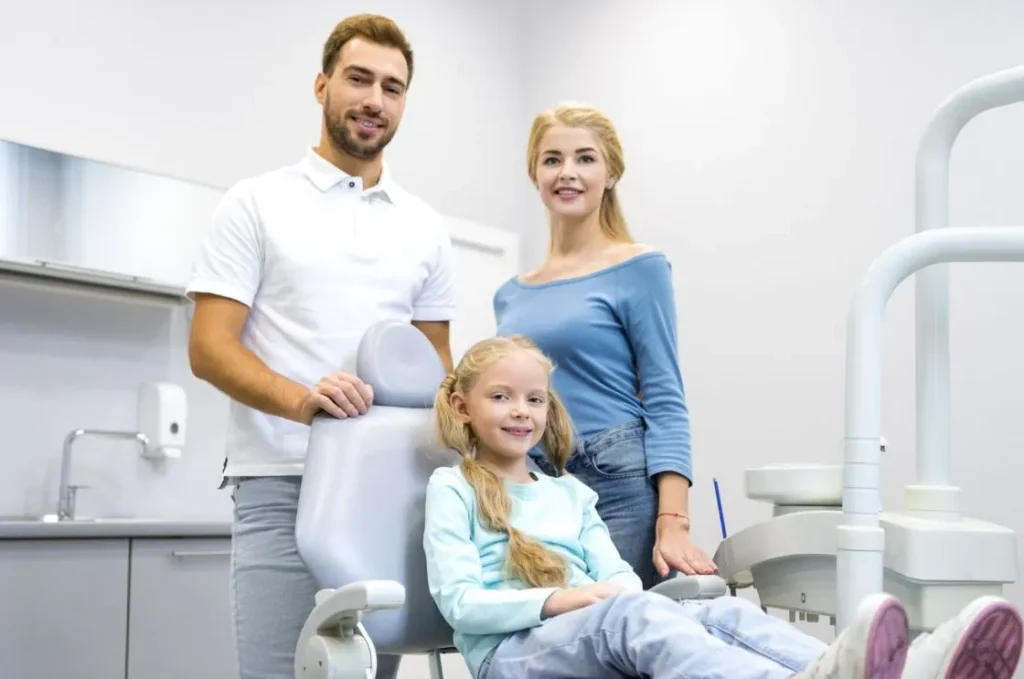 Mom and dad smiling next to a young girl in a dental exam chair.