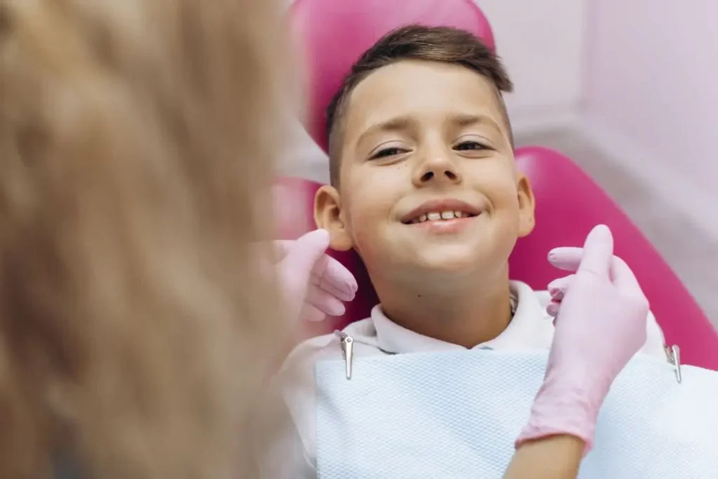 Young boy smiling while sitting in an exam chair beside a woman in medical gloves.